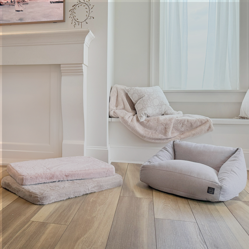 Fluffy pet beds in a home setting with a fireplace and window.