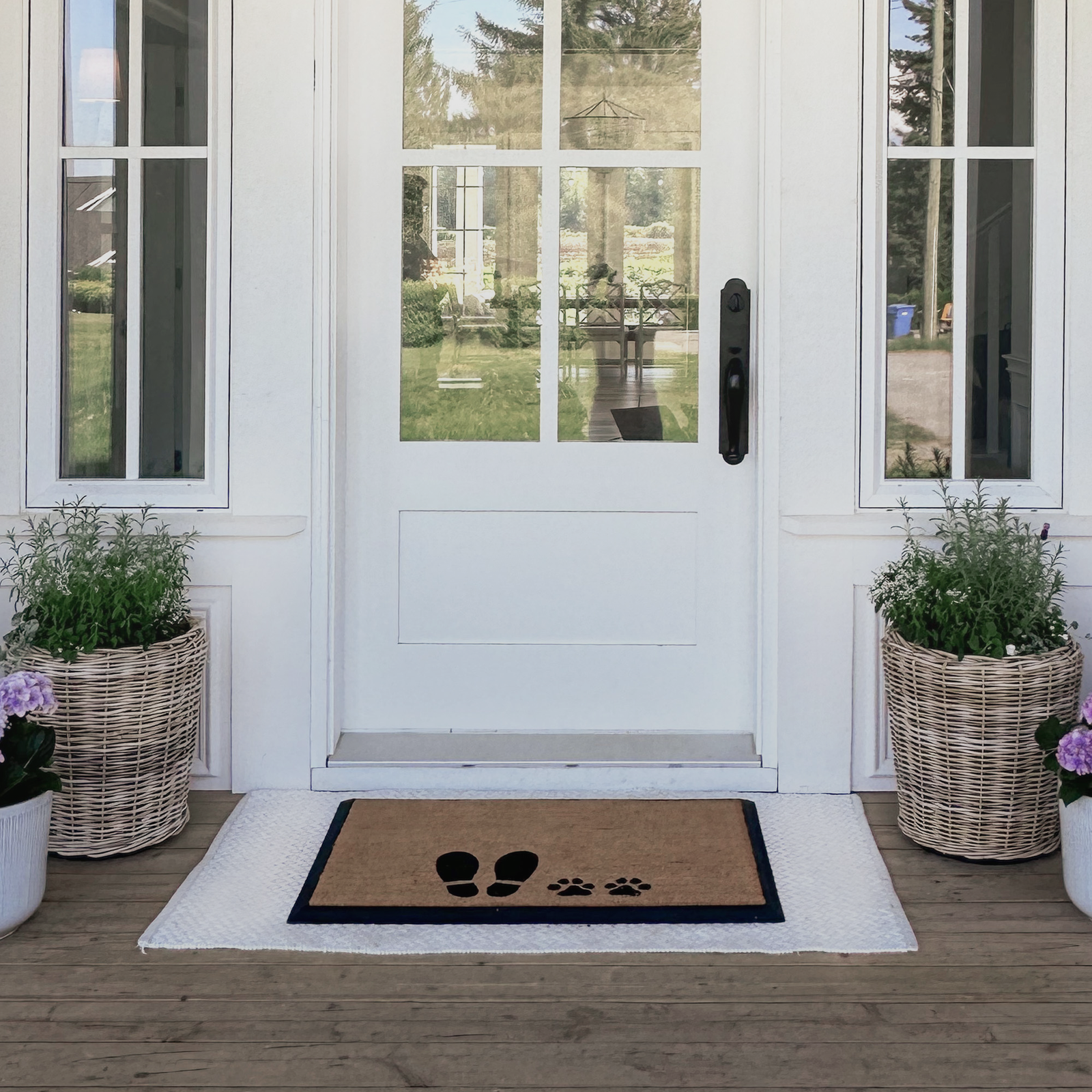 Doormat with paw prints on a wooden porch with plants and a glass door.